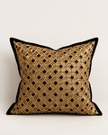 A square decorative throw pillow featuring a gold metallic geometric lattice pattern with black diamond cutouts, finished with a solid black velvet border, set against a plain light gray background.