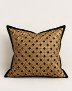 A square decorative throw pillow featuring a gold metallic geometric lattice pattern with black diamond cutouts, finished with a solid black velvet border, set against a plain light gray background.
