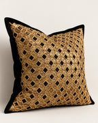 A square decorative throw pillow with a black velvet border and a gold metallic geometric lattice pattern on a light neutral background.