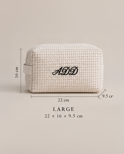 A textured cream-colored toiletry bag with a black monogram 'ADD' on the front, shown with dimension lines indicating its size as 22 x 16 x 9.5 cm, labeled as a LARGE size.