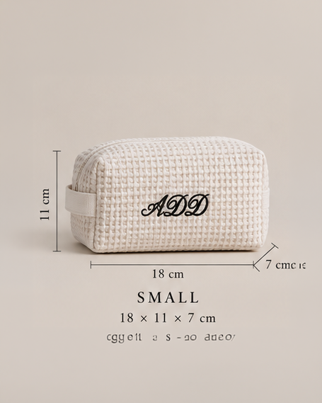 A small textured cream-colored cosmetic pouch with black monogrammed initials 'ADD' on the front, shown with dimension lines indicating measurements of 18 cm by 11 cm by 7 cm, on a solid beige background.