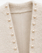Close-up of a cream-colored textured tweed jacket with a deep V-neckline adorned with a vertical row of round pearl buttons.