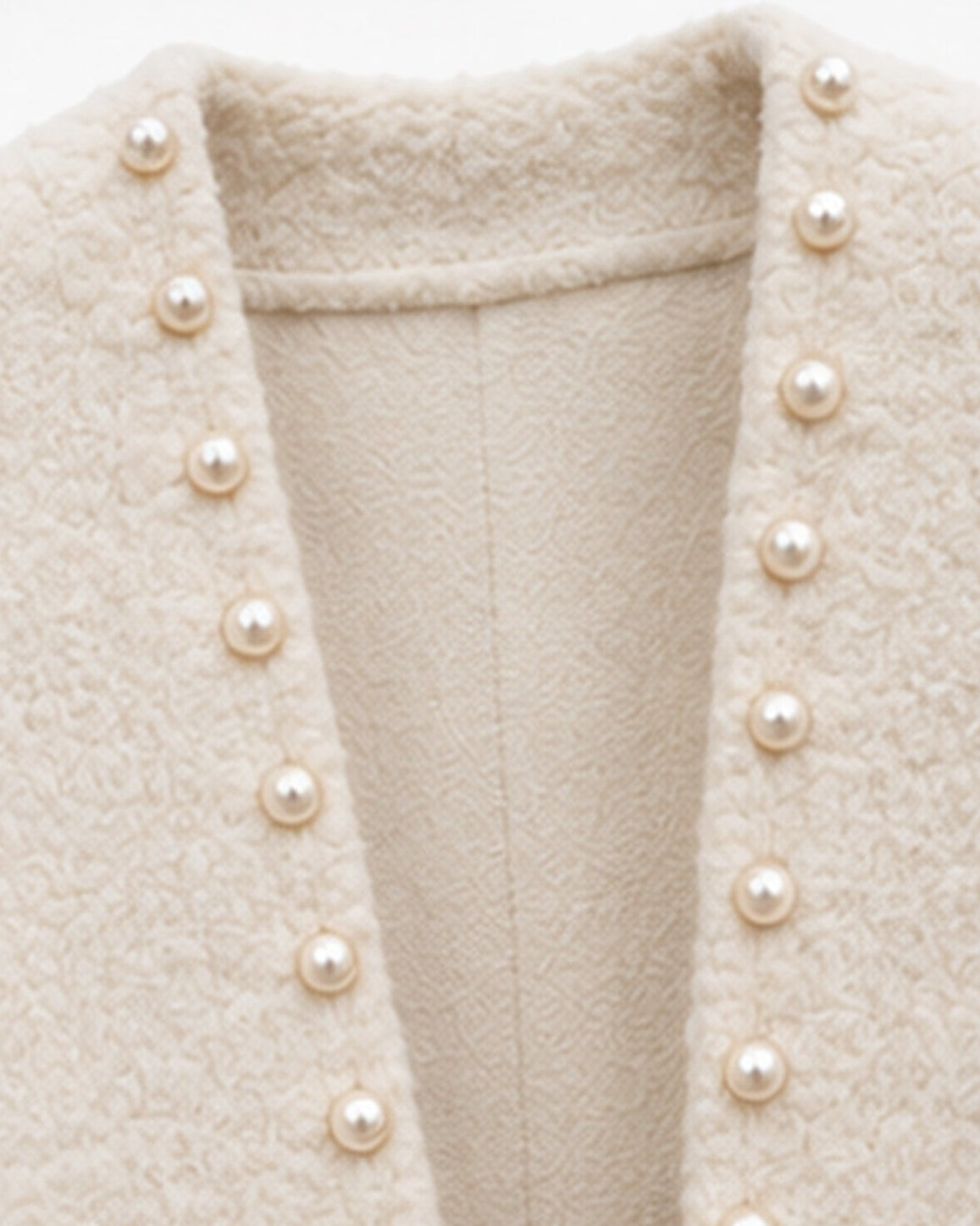 Close-up of a cream-colored textured tweed jacket with a deep V-neckline adorned with a vertical row of round pearl buttons.