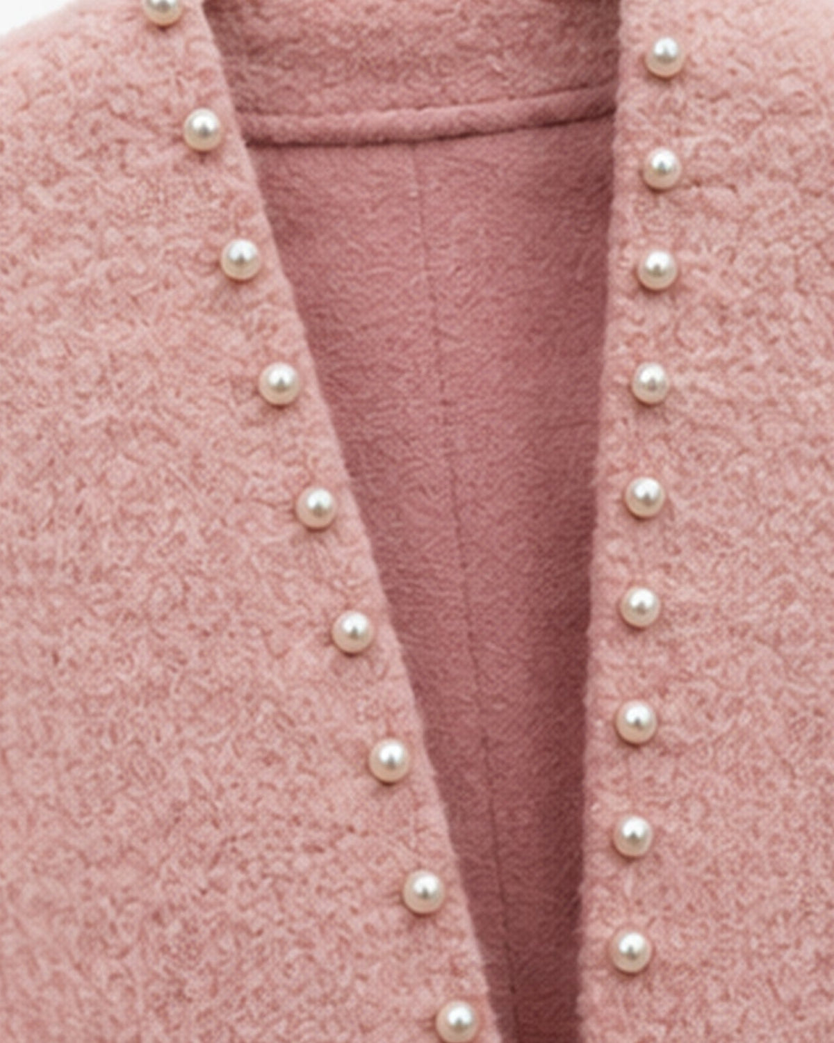 Close-up of a dusty pink textured cardigan featuring a deep V-neckline adorned with a vertical row of white faux-pearl buttons.