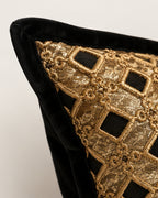 Close-up of a decorative throw pillow featuring a black velvet border and a gold embroidered geometric lattice pattern over a black fabric base.