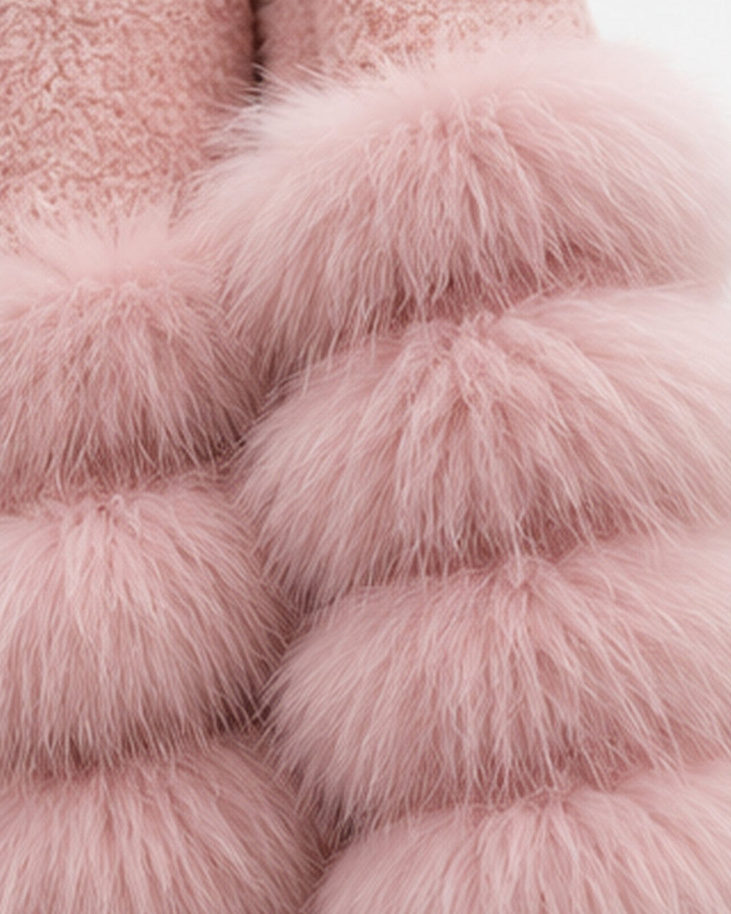 A close-up of a soft pink faux fur garment with layered, fluffy pom-pom style texture and a plush lining visible at the top, shown against a plain light background.
