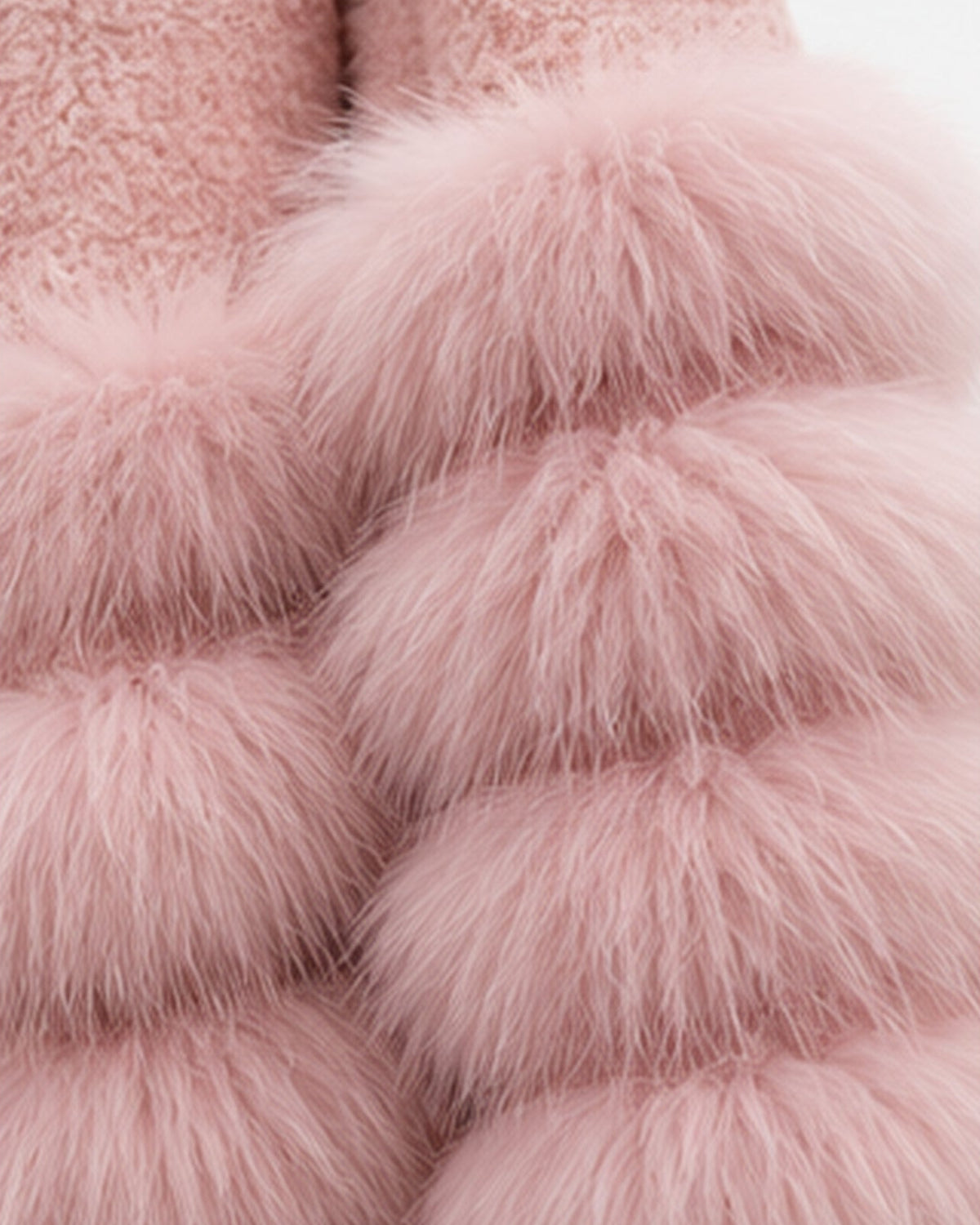 A close-up of a soft pink faux fur garment with layered, fluffy pom-pom style texture and a plush lining visible at the top, shown against a plain light background.