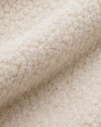 A close-up of a soft, textured cream-colored fabric with a looped or boucle-like surface, shown folded to highlight its plush texture.