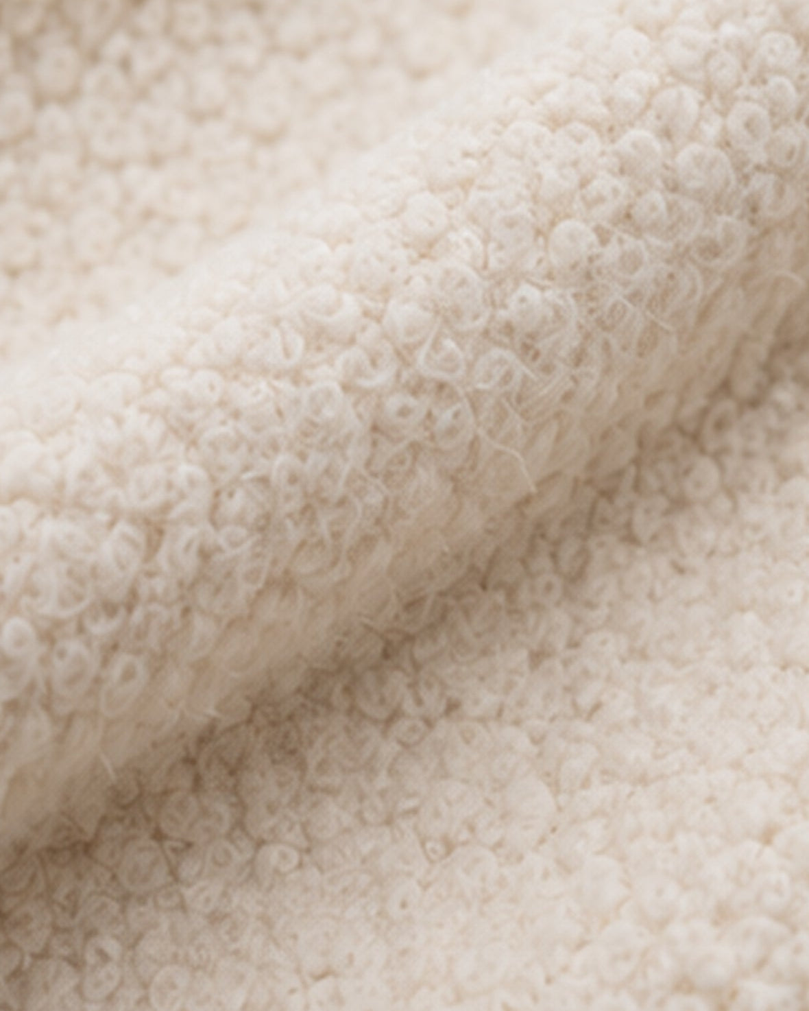 A close-up of a soft, textured cream-colored fabric with a looped or boucle-like surface, shown folded to highlight its plush texture.
