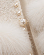 Close-up of a cream-colored textured jacket featuring fluffy white faux fur trim and a row of decorative pearl buttons.