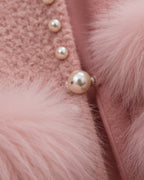 Close-up of a pink textured jacket with fluffy pink faux fur trim and decorative pearl buttons.