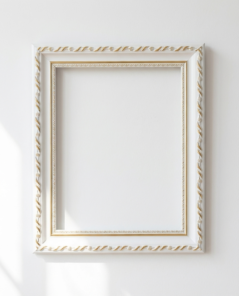 An ornate white picture frame with gold decorative detailing, shown hanging on a plain white wall with soft sunlight and shadows.