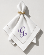 The Soirée Napkin with a purple embroidered initial, gathered in a gold napkin ring
