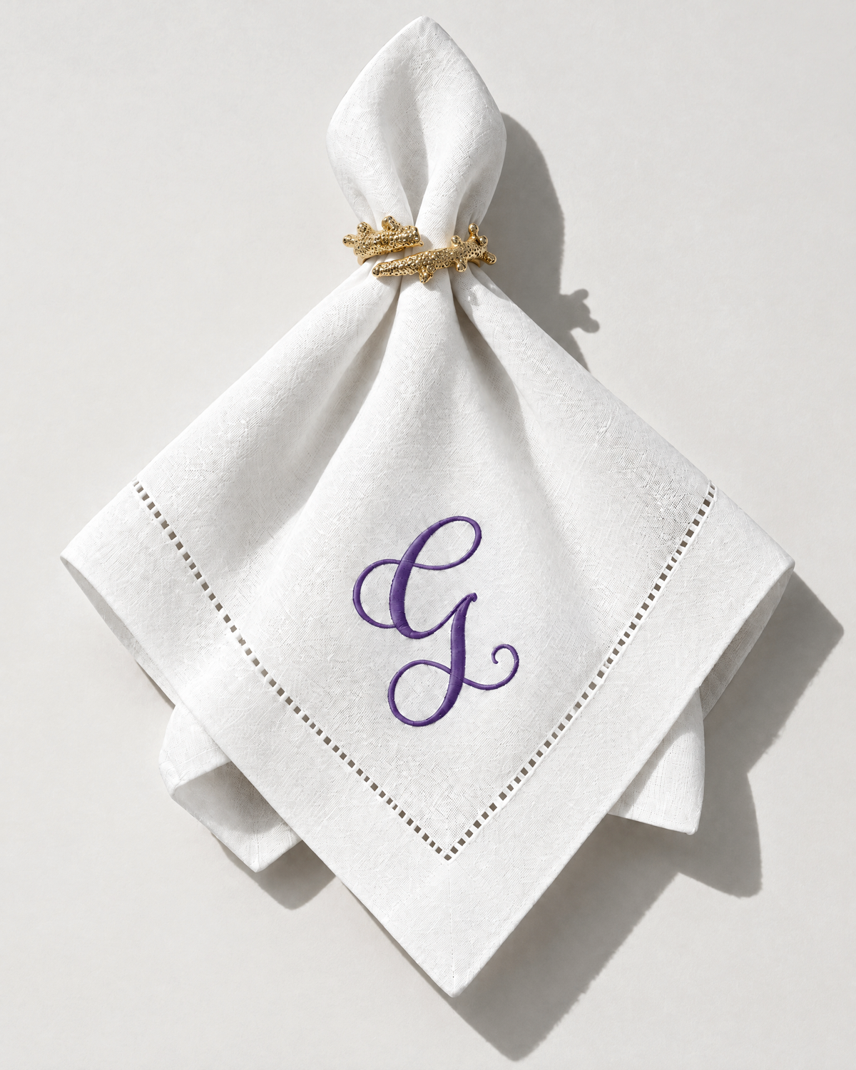 The Soirée Napkin with a purple embroidered initial, gathered in a gold napkin ring