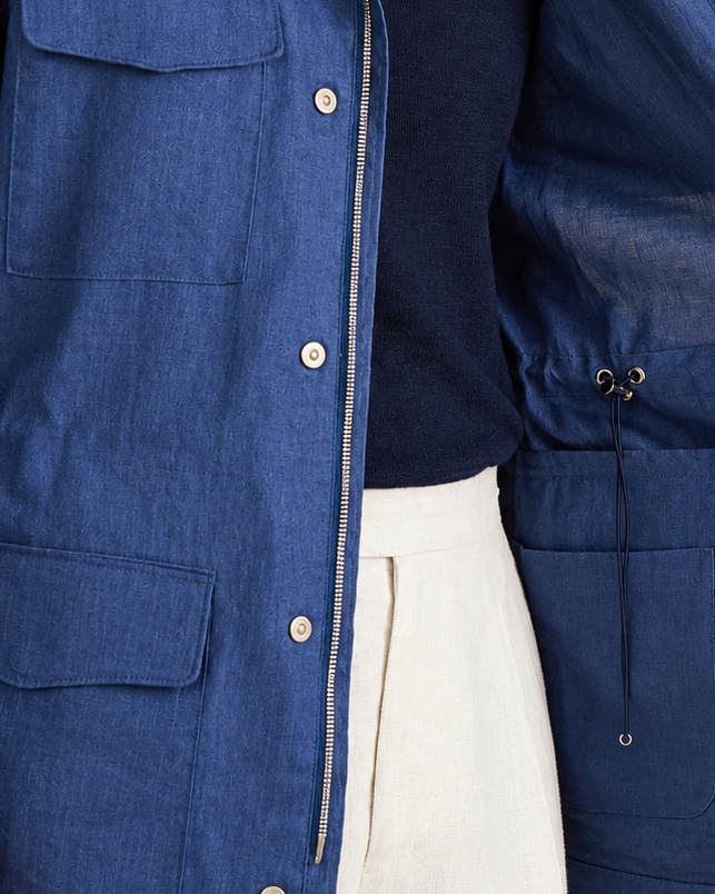 A person wearing a blue overshirt or jacket over a dark navy top and off-white trousers, shown from the chest down with the jacket open to reveal the interior pockets and lining.
