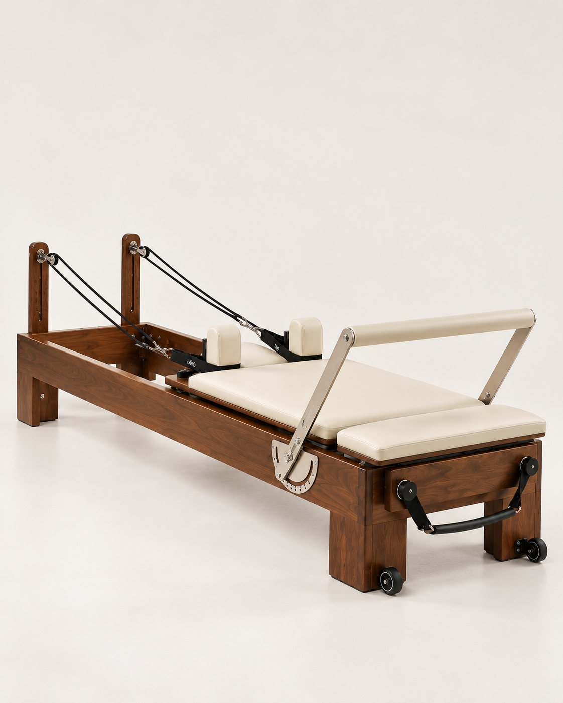 A wooden Pilates reformer machine with cream-colored padded straps and handlebar, set against a plain off-white studio background.