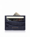 A navy blue crocodile-embossed cardholder wallet with gold 'THE CULT EDIT' branding, shown with credit cards and a dollar bill partially inserted, on a white background.
