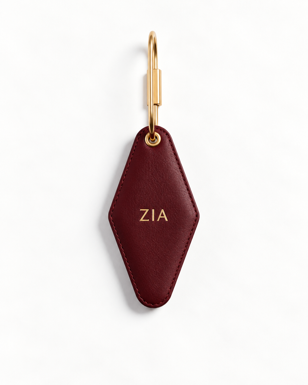 A burgundy leather keychain with a gold-tone metal key ring and a gold monogram 'ZIA' on a clean white background.