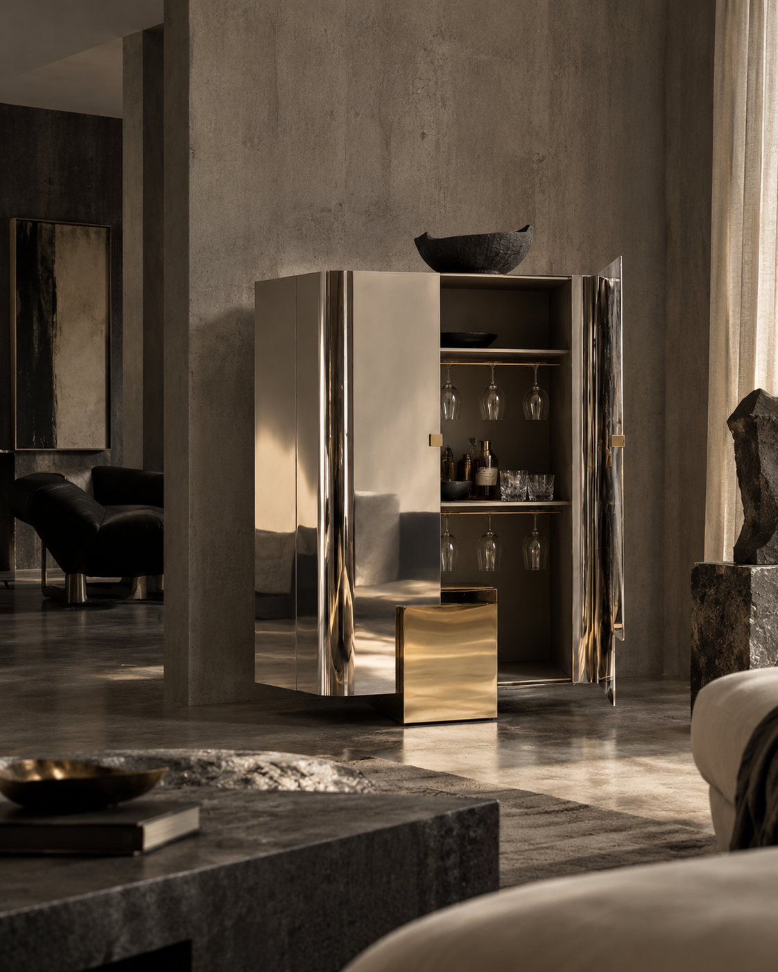A tall mirrored bar cabinet with gold-toned hardware stands in a modern, moody living room with concrete walls and warm sunlight streaming in.