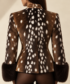A woman shown from the back wearing a brown fur jacket with a white spotted deer-print pattern and dark fur cuffs, against a plain beige studio background.