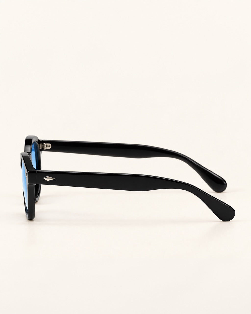 Black acetate sunglasses with a small silver logo on the temple arm, shown from a side profile view against a light cream background.