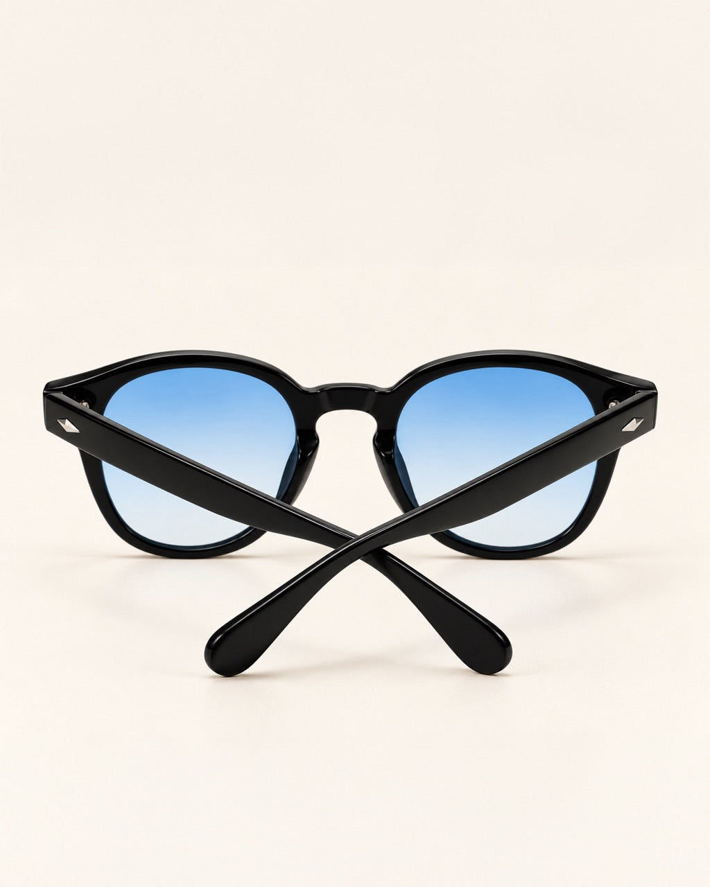 Black sunglasses with blue gradient lenses, shown crossed over each other on a light beige background.