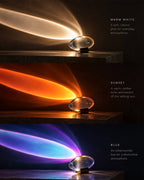 Three stacked product demonstration panels showing a clear oval crystal-like lamp on a small black stand, casting colored light beams in warm white, sunset orange, and blue modes, with descriptive text on a dark background.