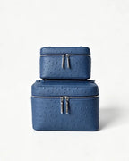 Two stacked blue textured leather cosmetic cases with silver zippers, photographed on a clean white background.