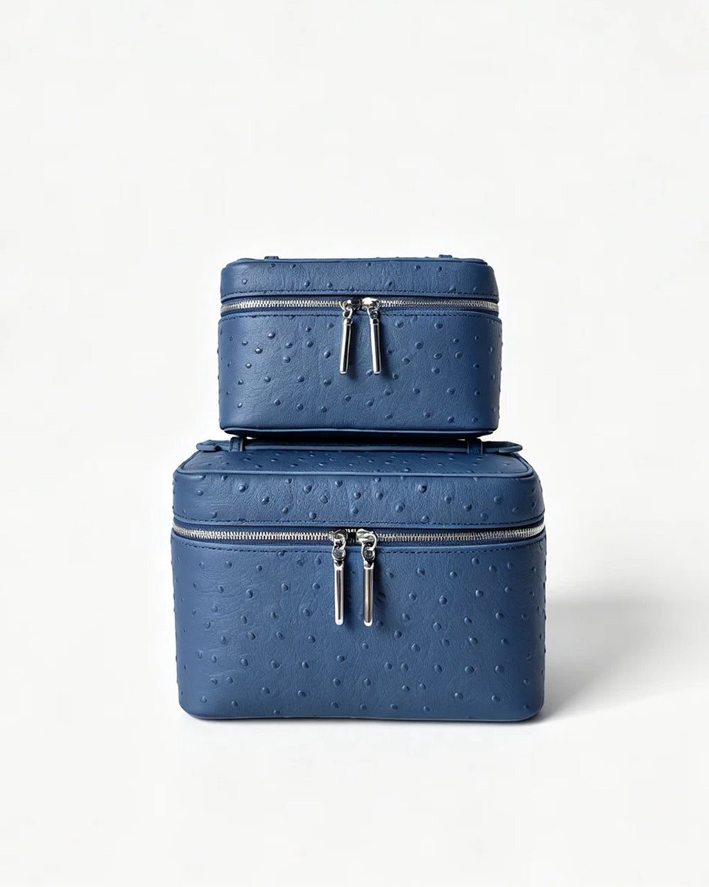 Two stacked blue textured leather cosmetic cases with silver zippers, photographed on a clean white background.