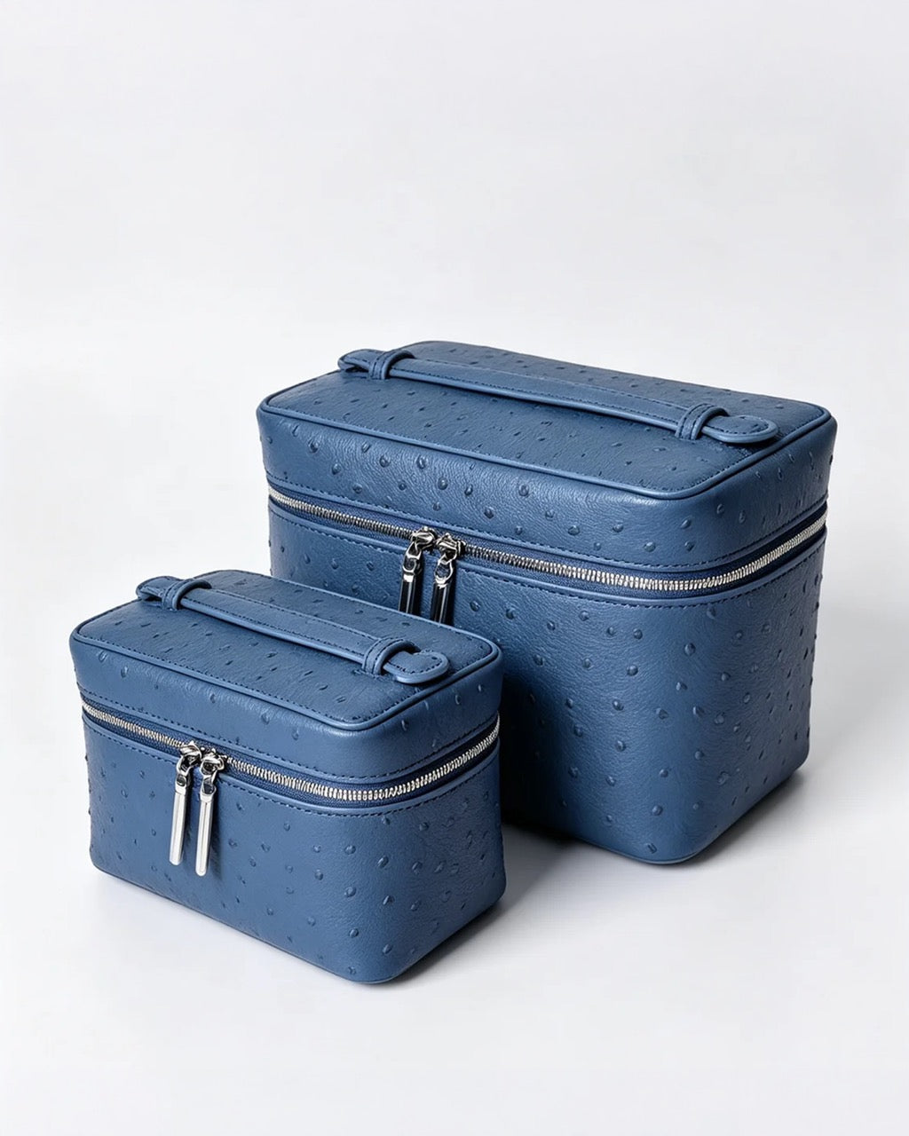 Two blue textured zippered cosmetic cases, one small and one large, made of an ostrich-embossed leather, shown on a light gray background.