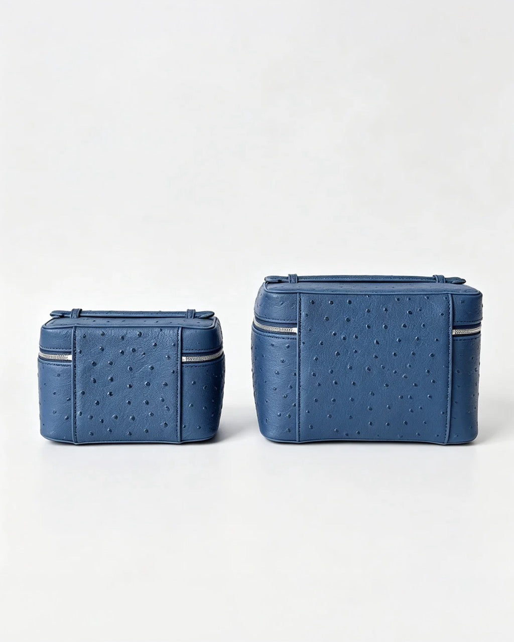 Two blue ostrich-textured leather cosmetic bags, one small and one large, displayed side-by-side on a clean white background.
