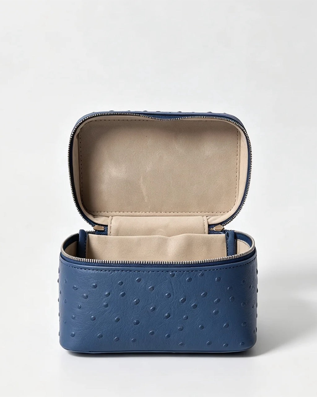 A blue textured faux-ostrich leather cosmetic case with an open lid, showing a beige interior lining, set against a plain light gray background.