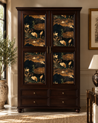 A tall dark wood armoire cabinet with four decorative doors featuring a gold and black nature print of deer and birds, set in a styled room with a window, potted plant, and lamp.