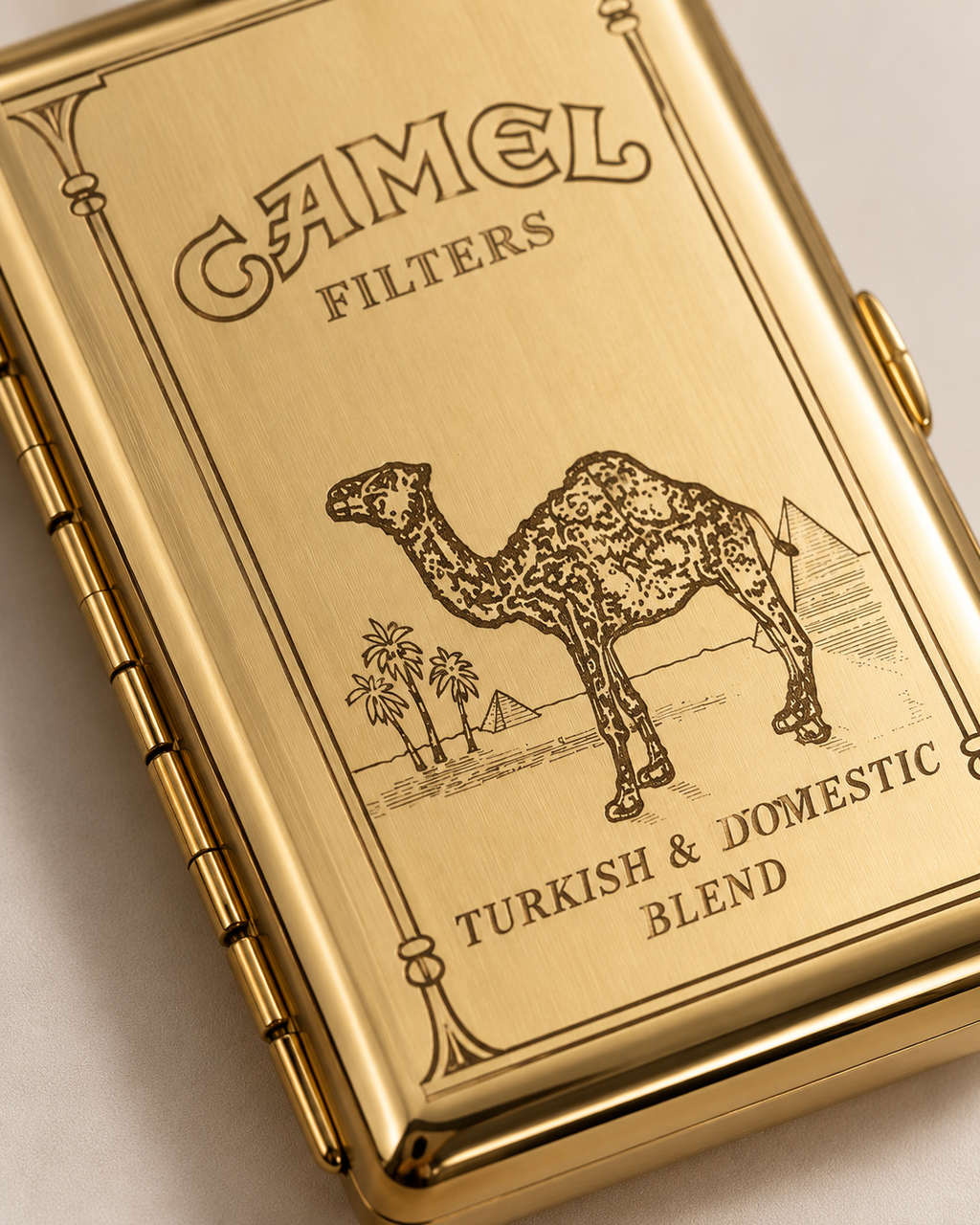 A close-up of a gold-toned Camel Filters cigarette case with an engraved camel and desert scene, plus the text 'Turkish & Domestic Blend'.