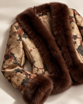 A close-up of a luxurious jacket featuring a dark brown fur collar and cuffs, paired with a beige brocade fabric decorated with floral patterns in brown, red, and black.