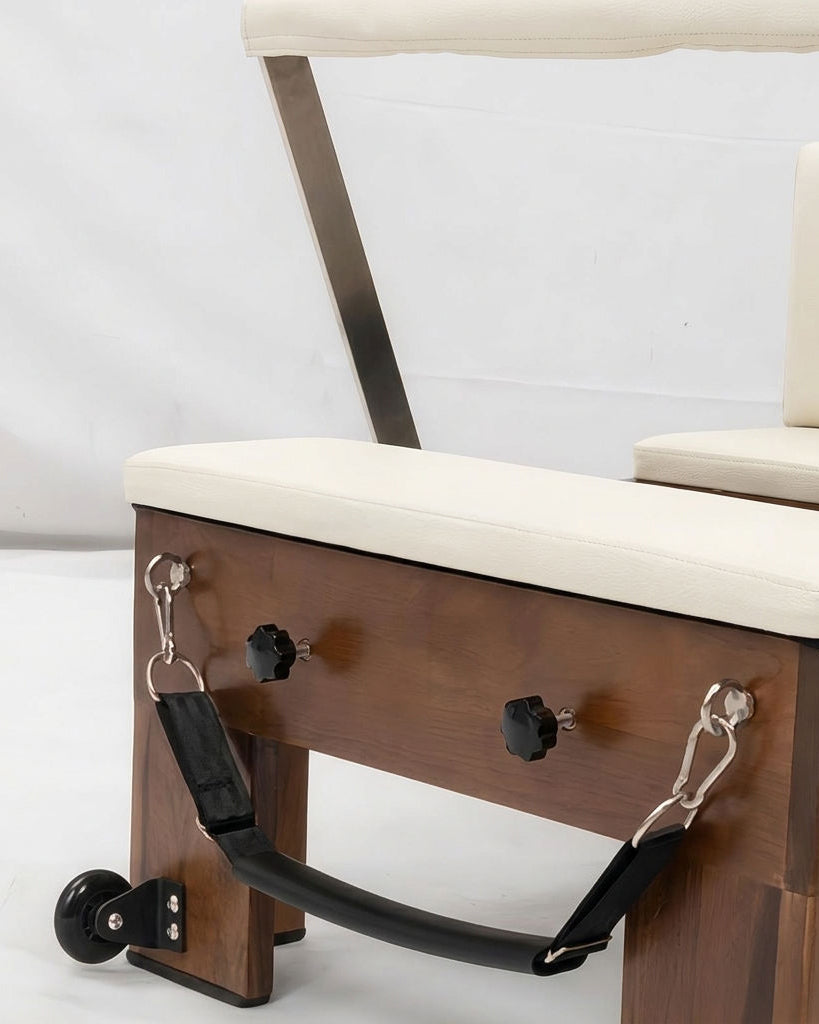 Close-up of a wooden exercise or therapy chair with cream upholstered seat and back, metal support frame, and black straps attached to the side.