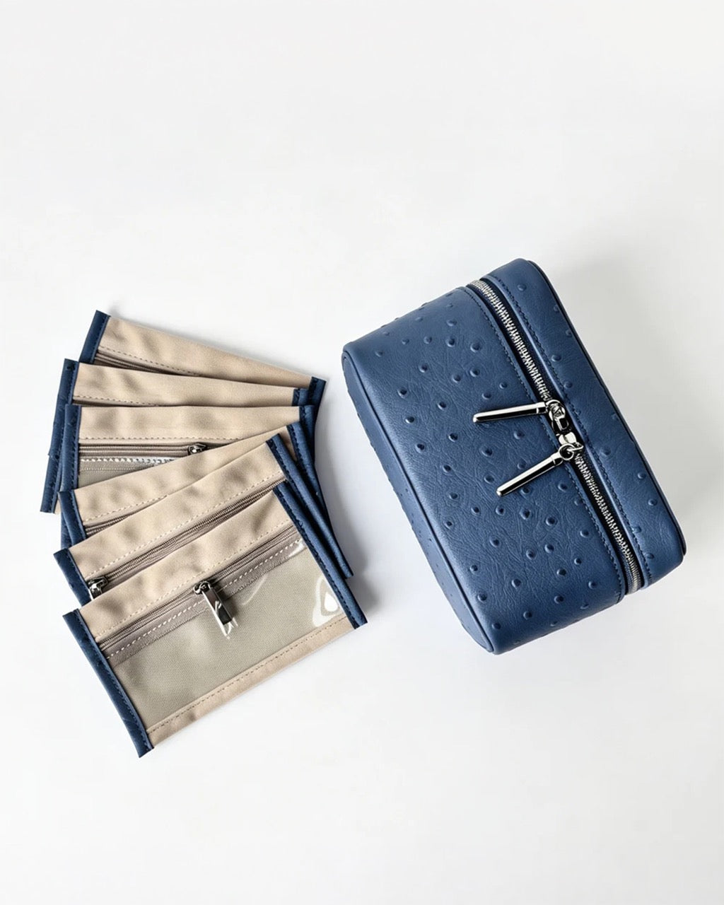 A blue textured zippered cosmetic pouch shown next to a fan of matching beige and blue zippered card slots on a clean white background.