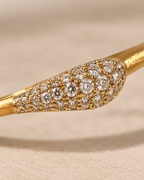 A close-up of a gold ring featuring a marquise-shaped pavé setting filled with round diamonds on a textured beige background.