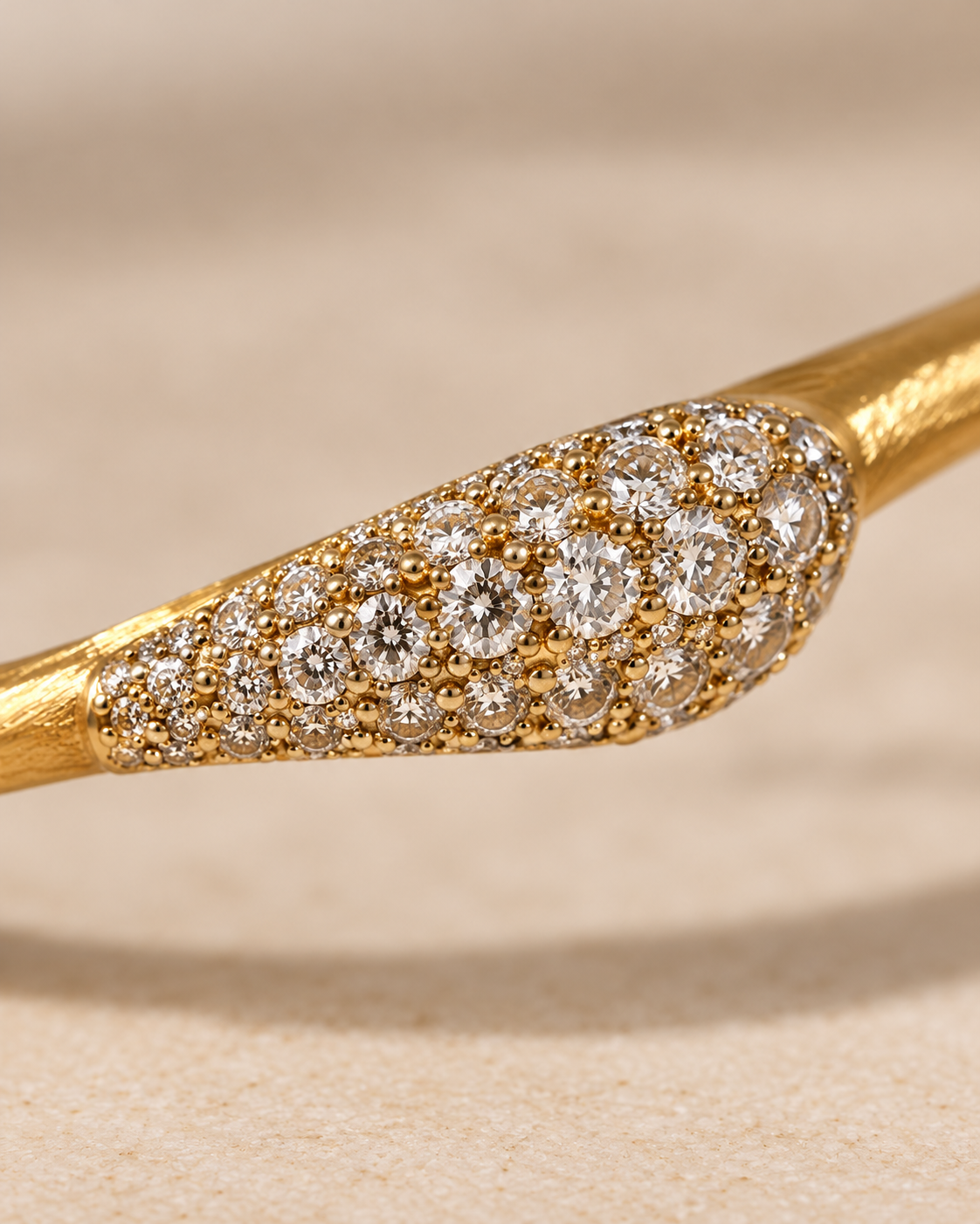 A close-up of a gold ring featuring a marquise-shaped pavé setting filled with round diamonds on a textured beige background.