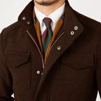 A close-up of a man wearing a dark brown textured jacket with silver snap buttons and a zipper, layered over a white dress shirt, a rust-orange patterned scarf, and a green and burgundy tie.