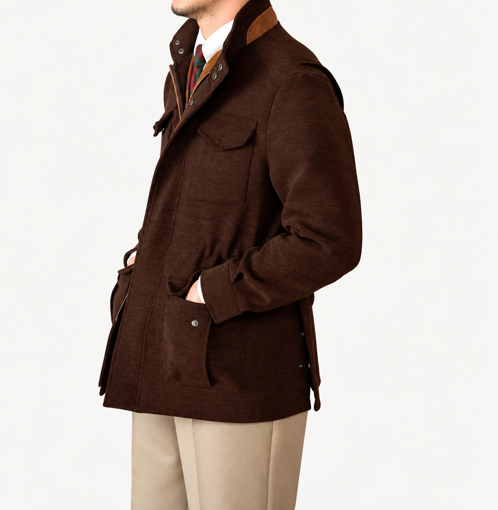 A man wearing a dark brown wool-blend jacket with brown corduroy collar and chest detail, paired with beige trousers and a patterned tie, shown in a side profile against a white studio background.