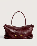 A burgundy crocodile-embossed leather handbag with a single top handle and gold-tone hardware, shown against a plain light gray background.