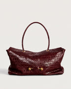 A burgundy crocodile-embossed leather handbag with a single top handle and gold-tone hardware, shown against a plain light gray background.