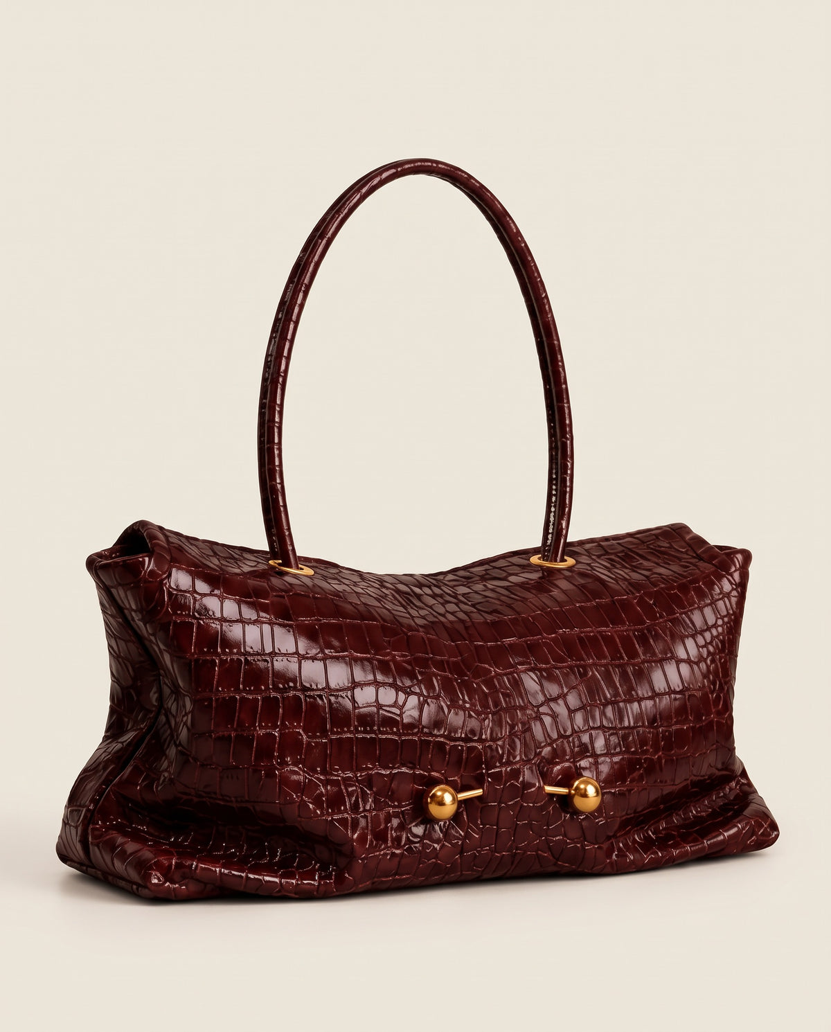 A burgundy crocodile-embossed leather handbag with dual top handles and gold-tone hardware, shown against a solid light beige background.