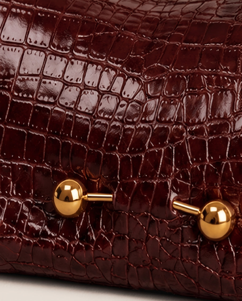 Close-up of a dark burgundy crocodile-embossed leather bag with shiny gold-tone metal hardware.