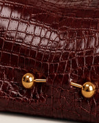 Close-up of a dark burgundy crocodile-embossed leather bag with shiny gold-tone metal hardware.