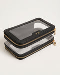 A black faux-leather zippered pouch with a clear window on top and a second clear zippered layer underneath, featuring gold zippers and a gold monogram 'PS' on the clear window.