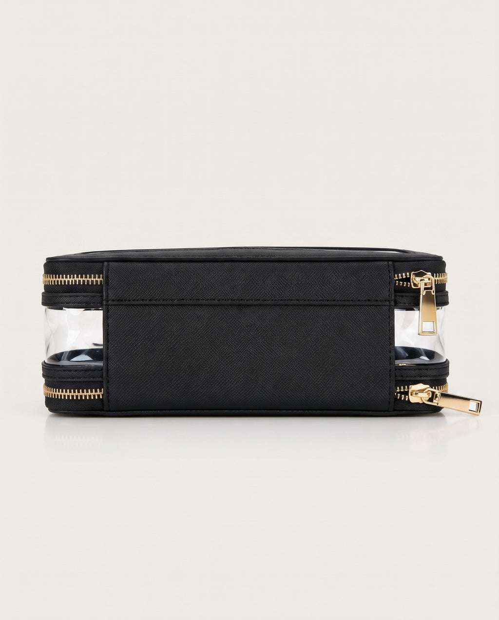 A black rectangular zippered pouch with clear plastic side panels and gold-tone zippers, shown on a light gray studio background.