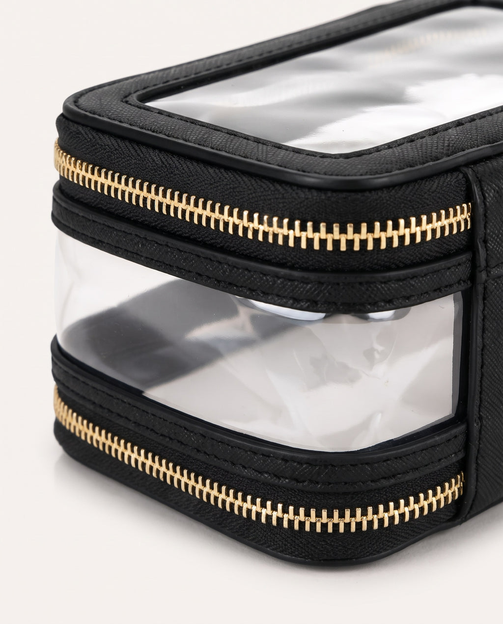 Black textured toiletry bag with clear plastic windows and gold-tone zippers, shown in a close-up studio shot on a light background.