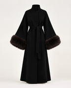 A long black wrap coat with a high collar, wide sleeves, and dark brown fur trim at the cuffs, shown on a plain light background.